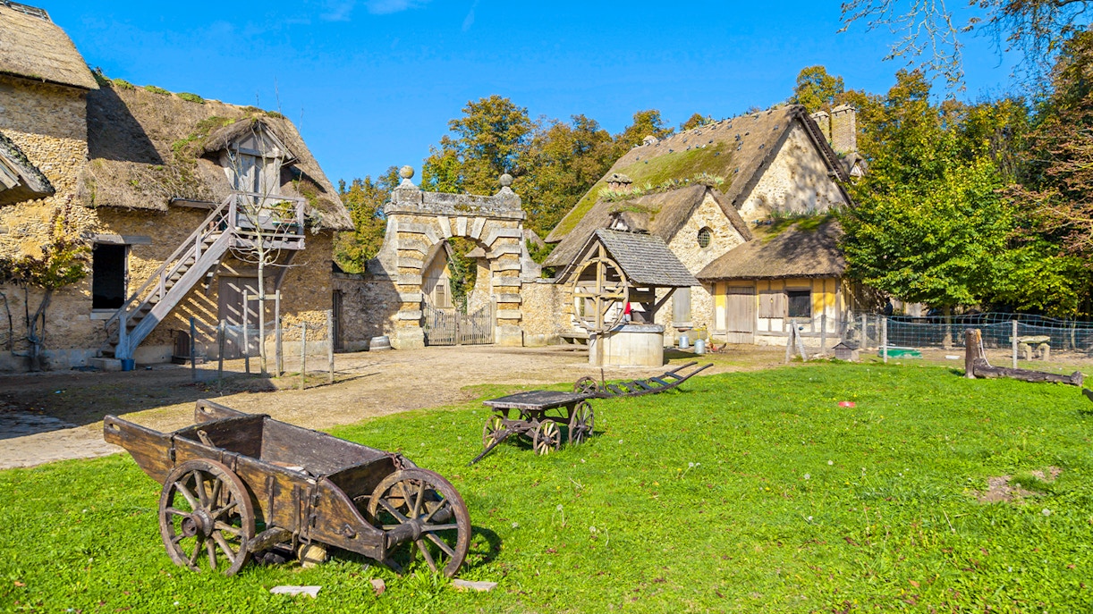Rustic village scene at Marie-Antoinette's Domain, Versailles, with stone cottages and wooden carts.