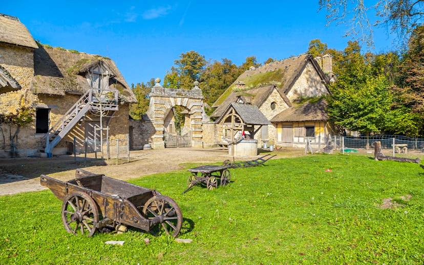 Rustic village scene at Marie-Antoinette's Domain, Versailles, with stone cottages and wooden carts.