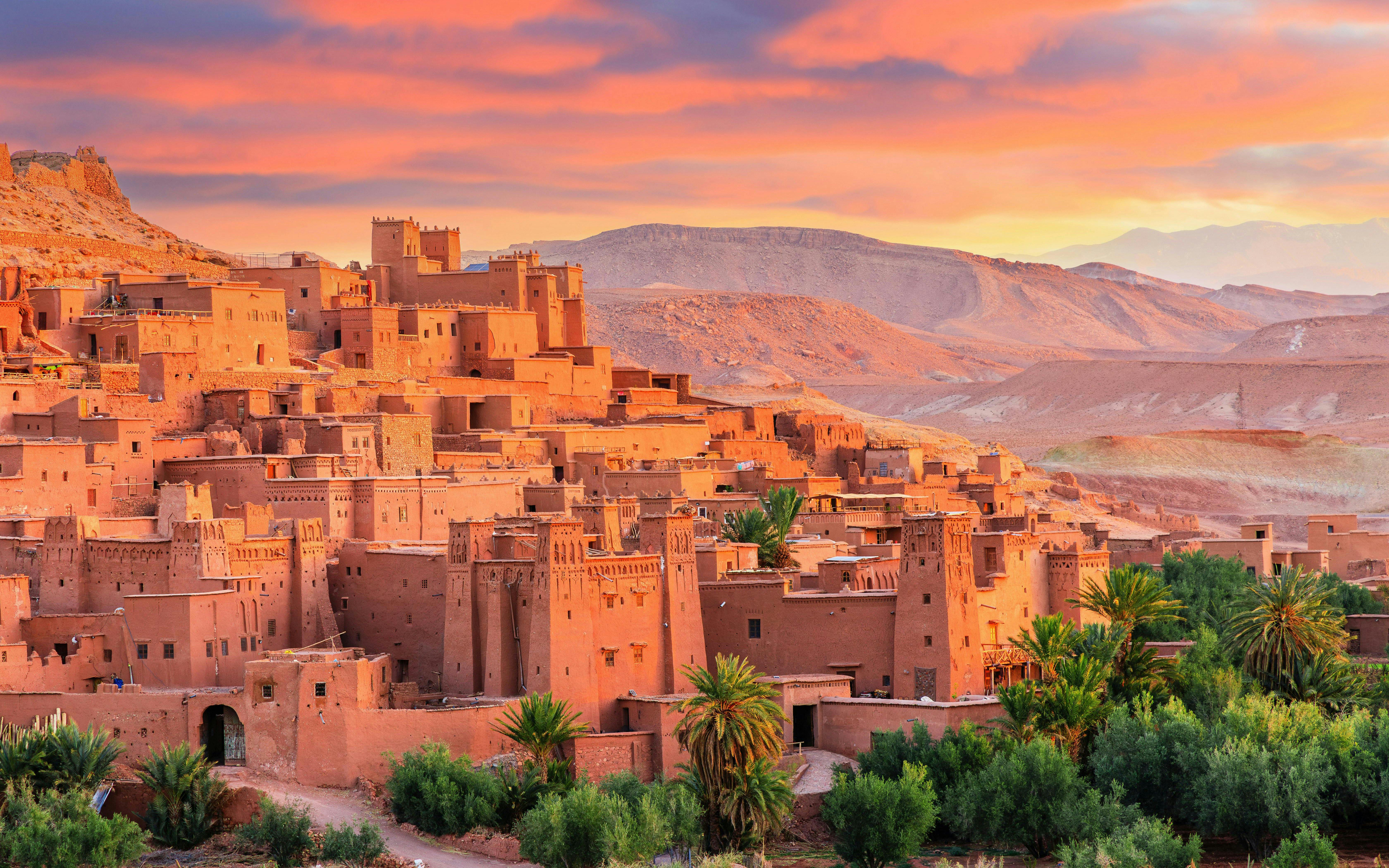 Ait Ben Haddou kasbah with clay buildings and palm trees at sunset, Morocco.