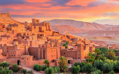 Ait Ben Haddou kasbah with clay buildings and palm trees at sunset, Morocco.