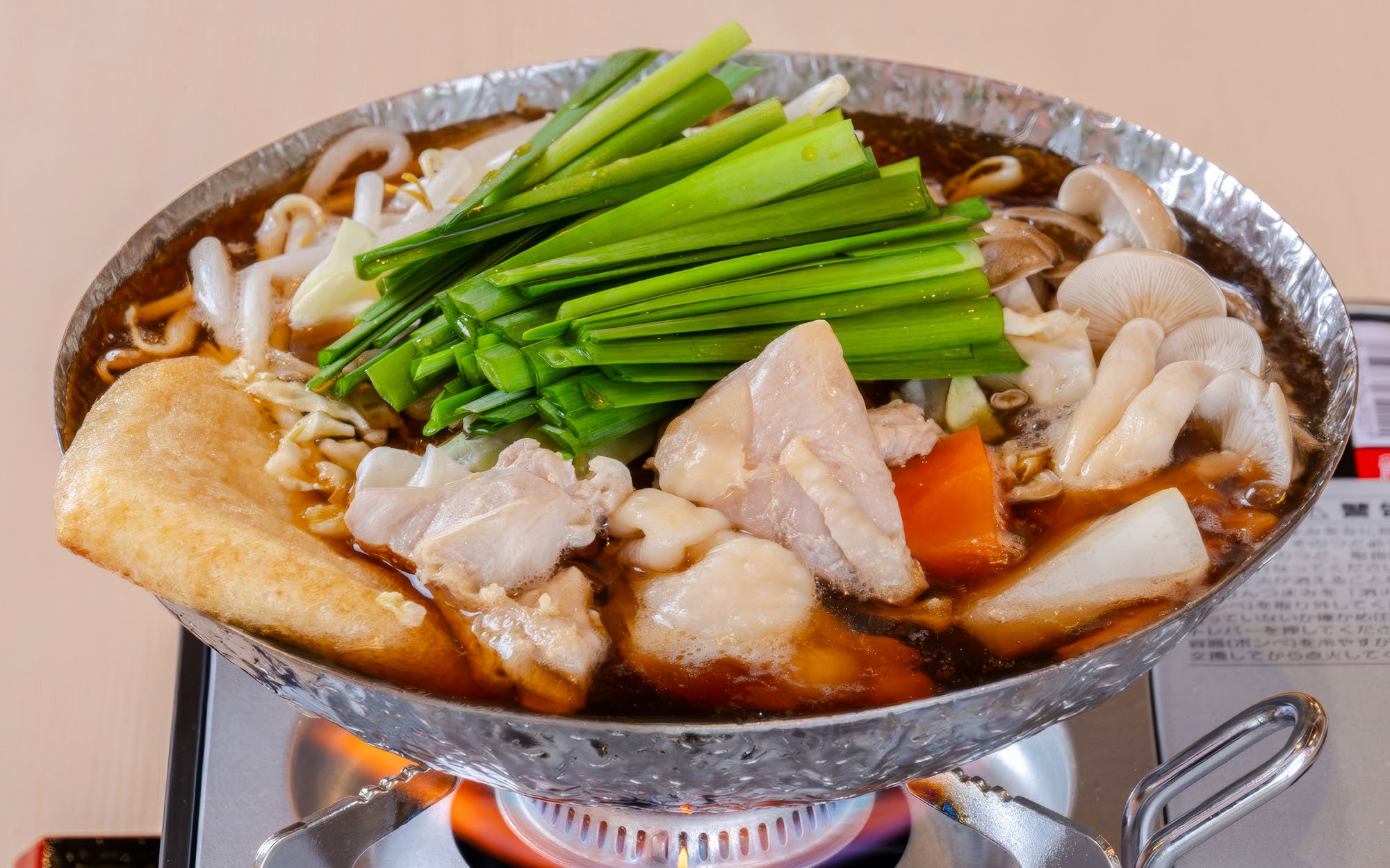 Chankonabe hot pot with chicken, vegetables, and mushrooms on a stove.