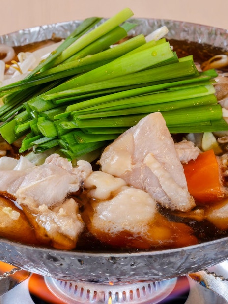 Chankonabe hot pot with chicken, vegetables, and mushrooms on a stove.