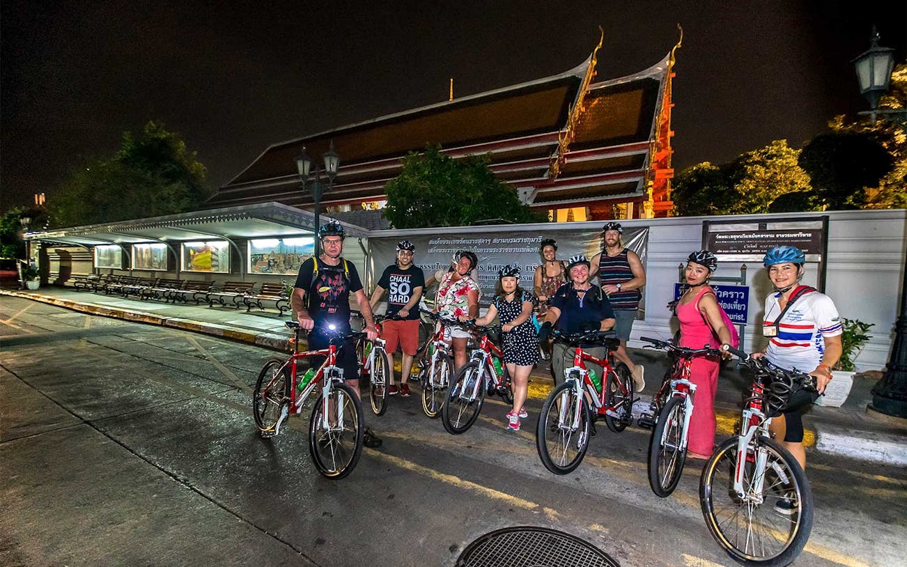 Group of cyclists on a night tour in front of a temple in Bangkok.