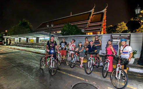 Group of cyclists on a night tour in front of a temple in Bangkok.