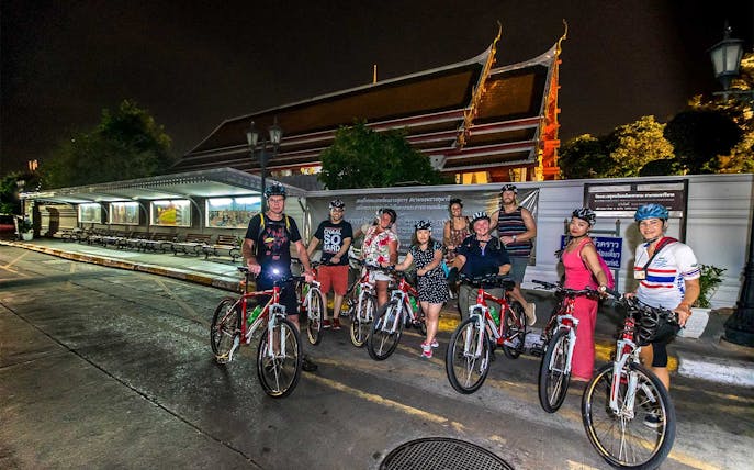 Group of cyclists on a night tour in front of a temple in Bangkok.