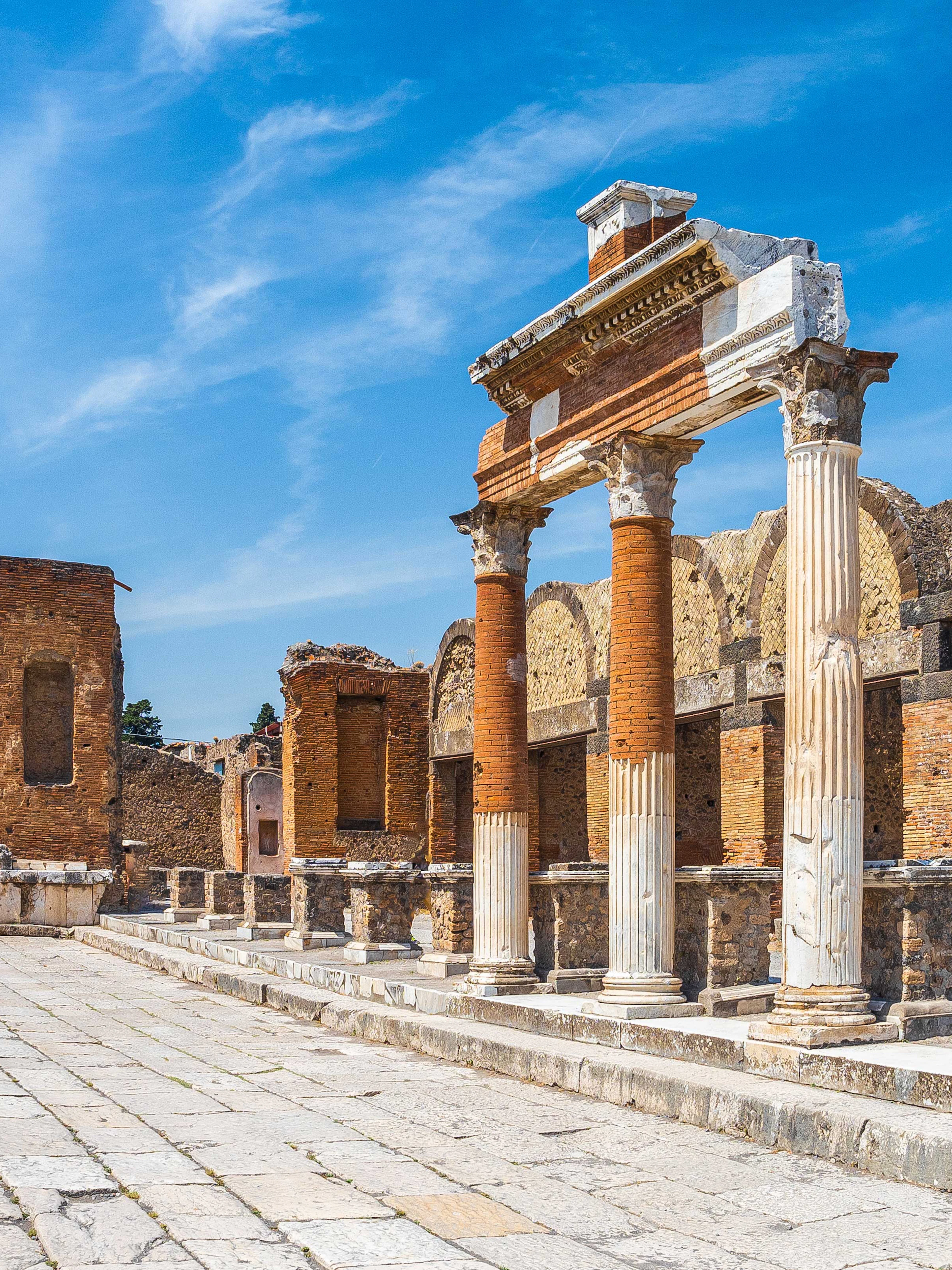 Ancient ruins of Pompeii with columns and archway under a clear blue sky.
