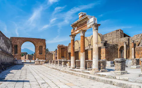 Ancient ruins of Pompeii with columns and archway under a clear blue sky.