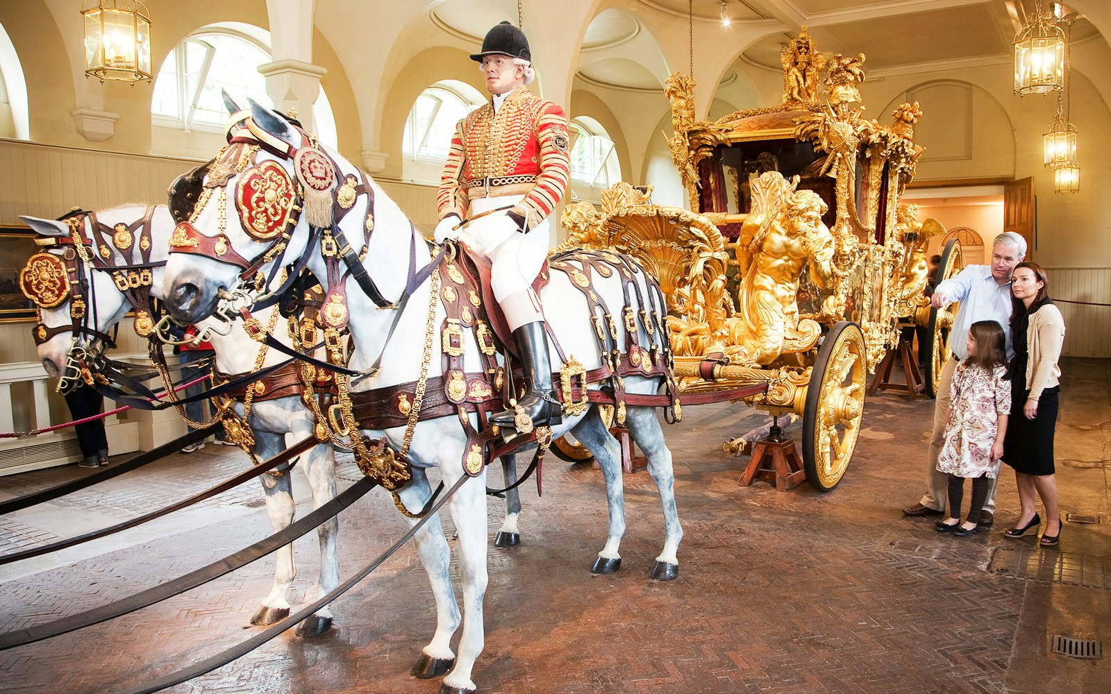 Royal Mews at Buckingham Palace with ornate carriage and horses, guide explaining to visitors.