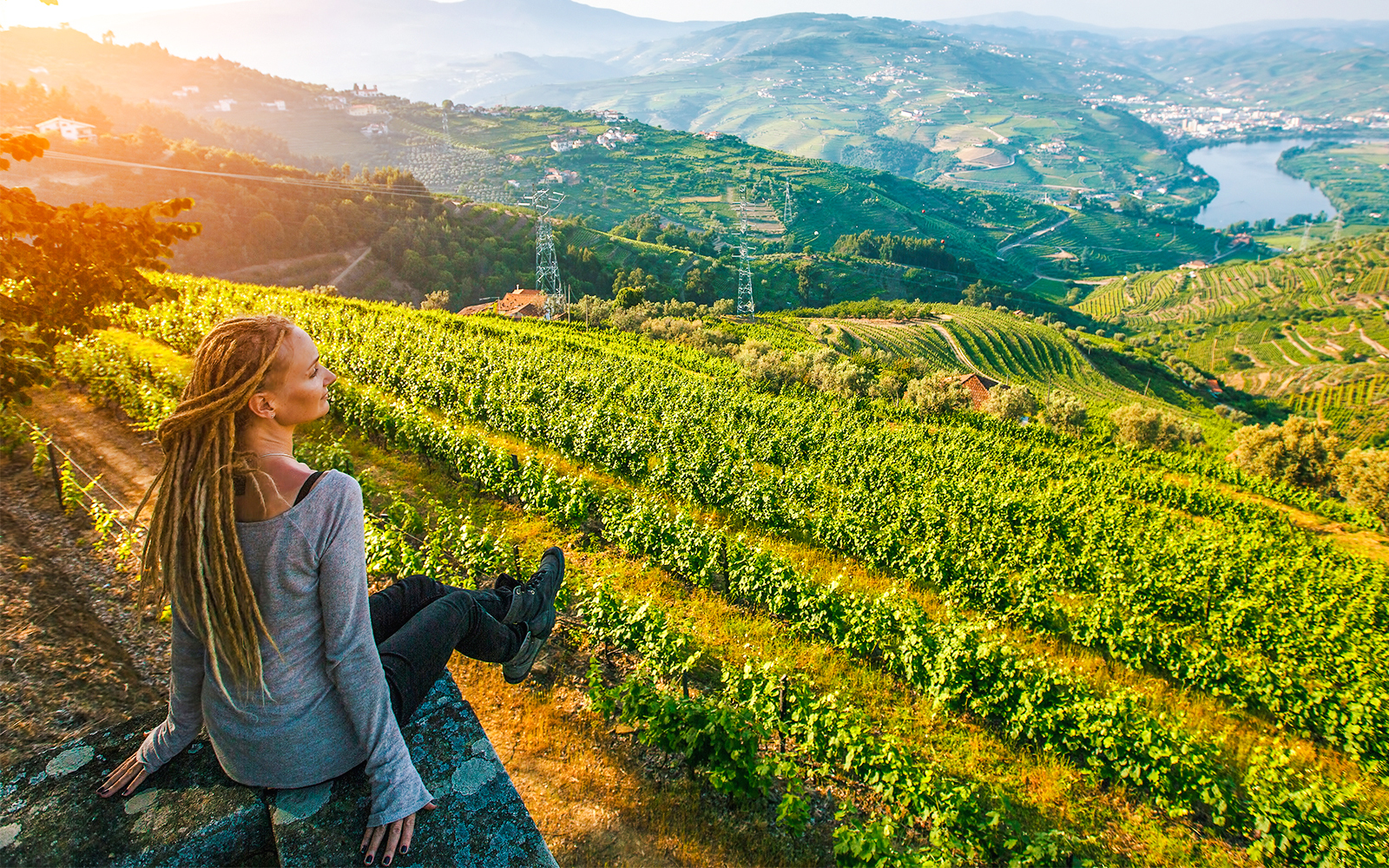 Woman sitting on a stone wall overlooking vineyards in Douro Valley, Portugal.