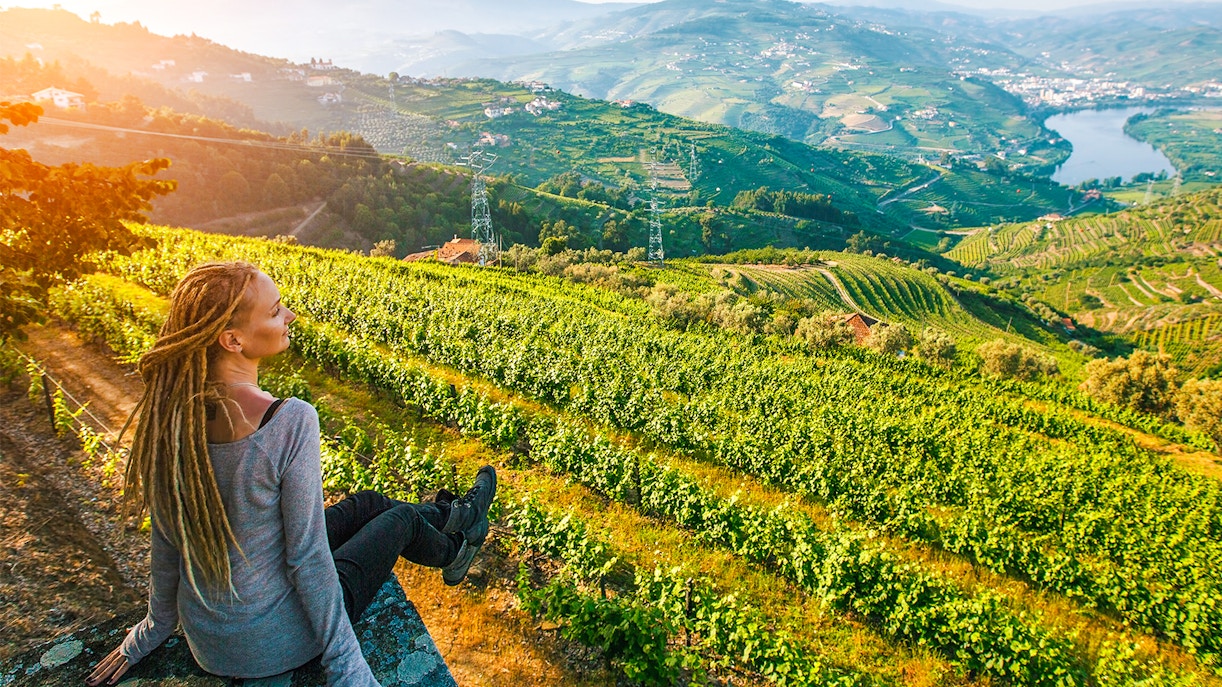Woman sitting on a stone wall overlooking vineyards in Douro Valley, Portugal.