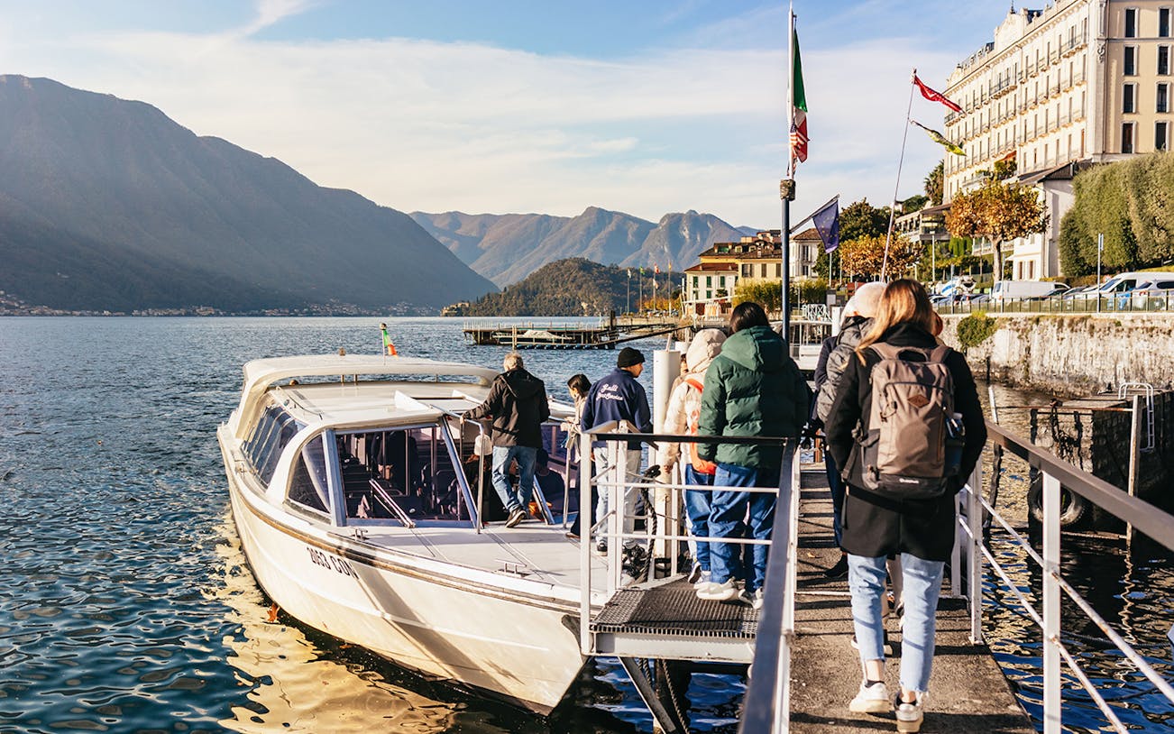 Scenic view of Lake Como with a cruise boat, surrounded by mountains, part of the Como Cruise, St. Moritz & Bernina Red Train tour.