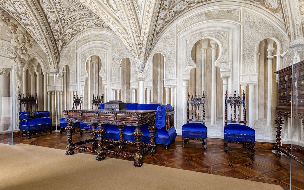 Ornate sitting room in Pena Palace with carved wooden furniture and blue upholstery.