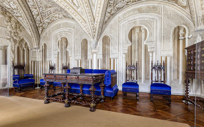 Ornate sitting room in Pena Palace with carved wooden furniture and blue upholstery.