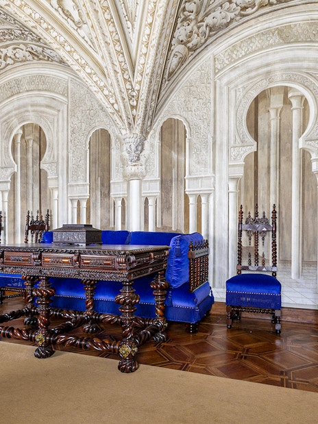 Ornate sitting room in Pena Palace with carved wooden furniture and blue upholstery.