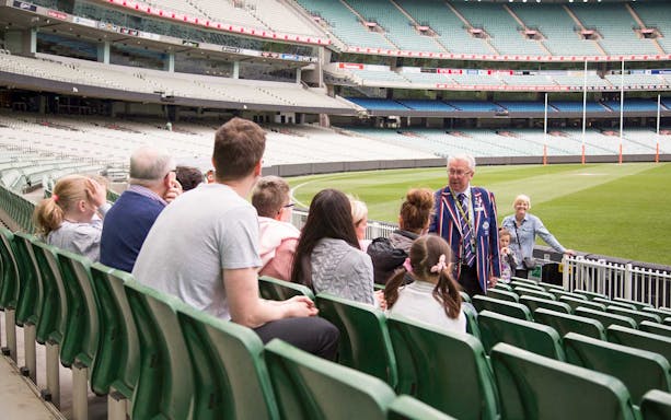 Tour group at Melbourne Cricket Ground with guide explaining stadium features.