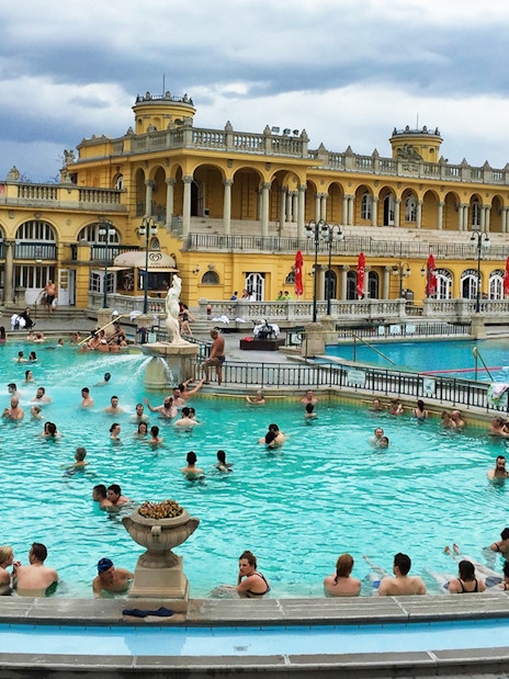 Visitors enjoying thermal pools at Szechenyi Bath, Budapest, with historic architecture in the background.