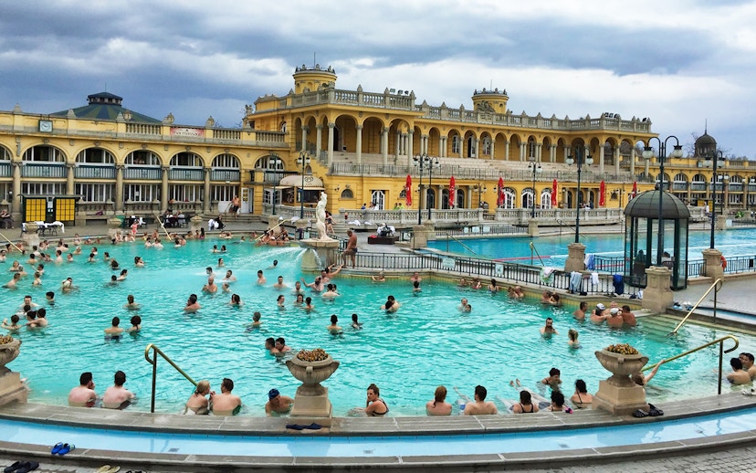 Visitors enjoying thermal pools at Szechenyi Bath, Budapest, with historic architecture in the background.