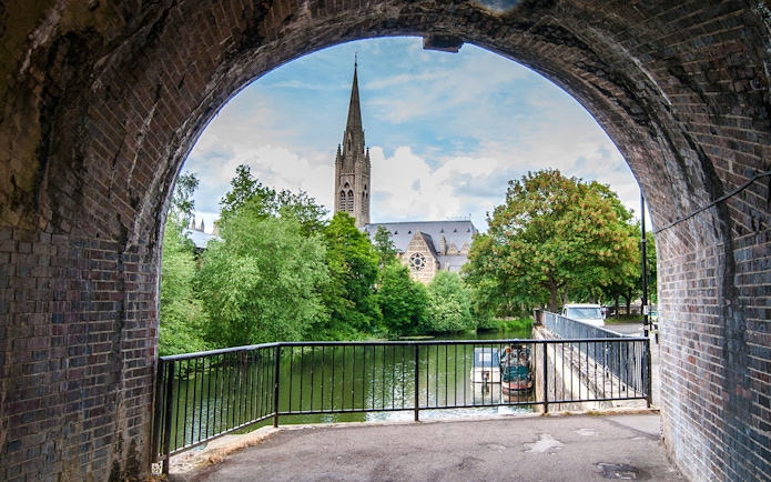 View of St John the Evangelist's Church spire through a stone archway in Bath, England.