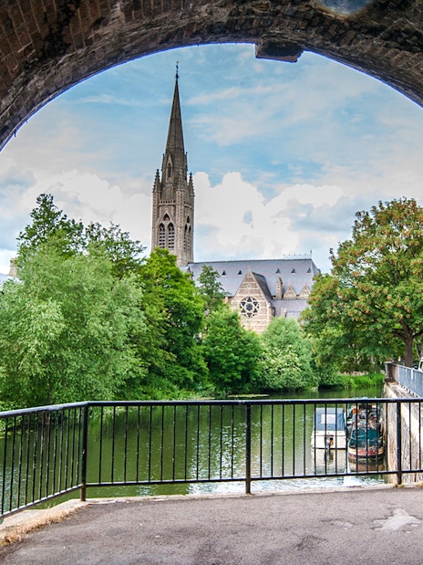 View of St John the Evangelist's Church spire through a stone archway in Bath, England.