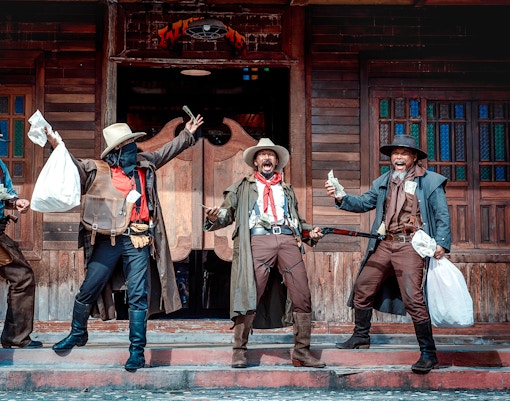 Cowboys performing a Wild West show with money and props in front of a saloon.