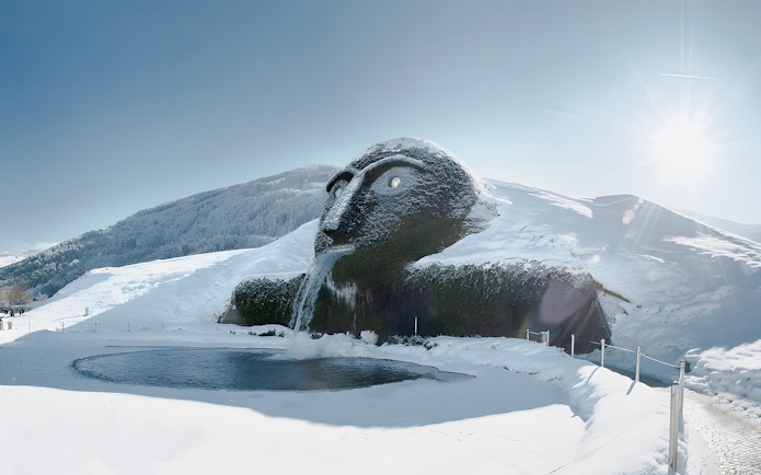 Giant head sculpture with waterfall at Swarovski Crystal Worlds, Austria, in snowy landscape.