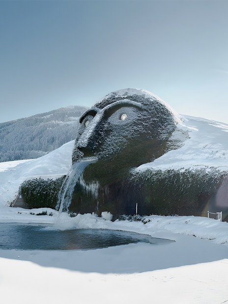 Giant head sculpture with waterfall at Swarovski Crystal Worlds, Austria, in snowy landscape.