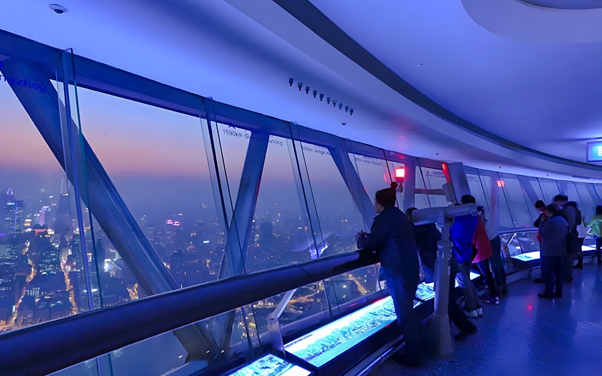 Visitors at the Oriental Pearl Tower observation deck, Shanghai, viewing city skyline.
