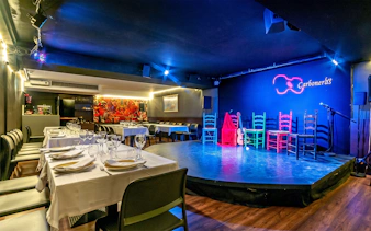 Flamenco stage setup at Tablao LAS CARBONERAS with colorful chairs and guitar.