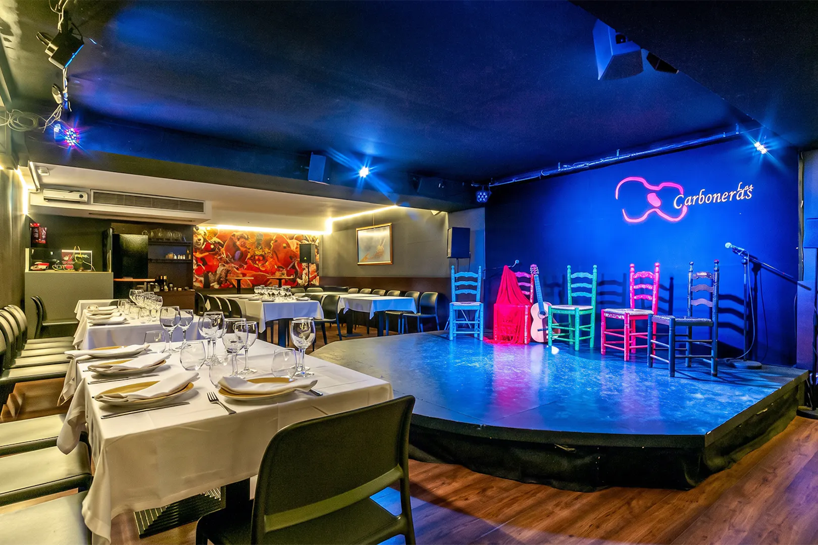 Flamenco stage setup at Tablao LAS CARBONERAS with colorful chairs and guitar.