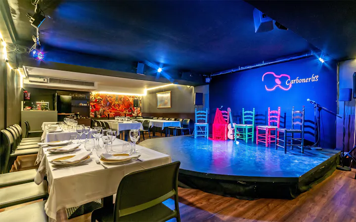 Flamenco stage setup at Tablao LAS CARBONERAS with colorful chairs and guitar.