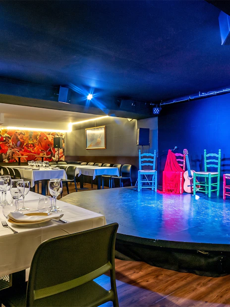Flamenco stage setup at Tablao LAS CARBONERAS with colorful chairs and guitar.