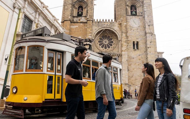 Tram passing by Lisbon Cathedral with tourists walking nearby.