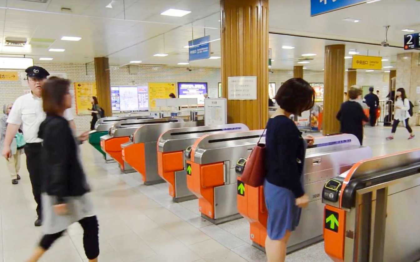 Fukuoka City subway turnstiles with passengers entering the station.