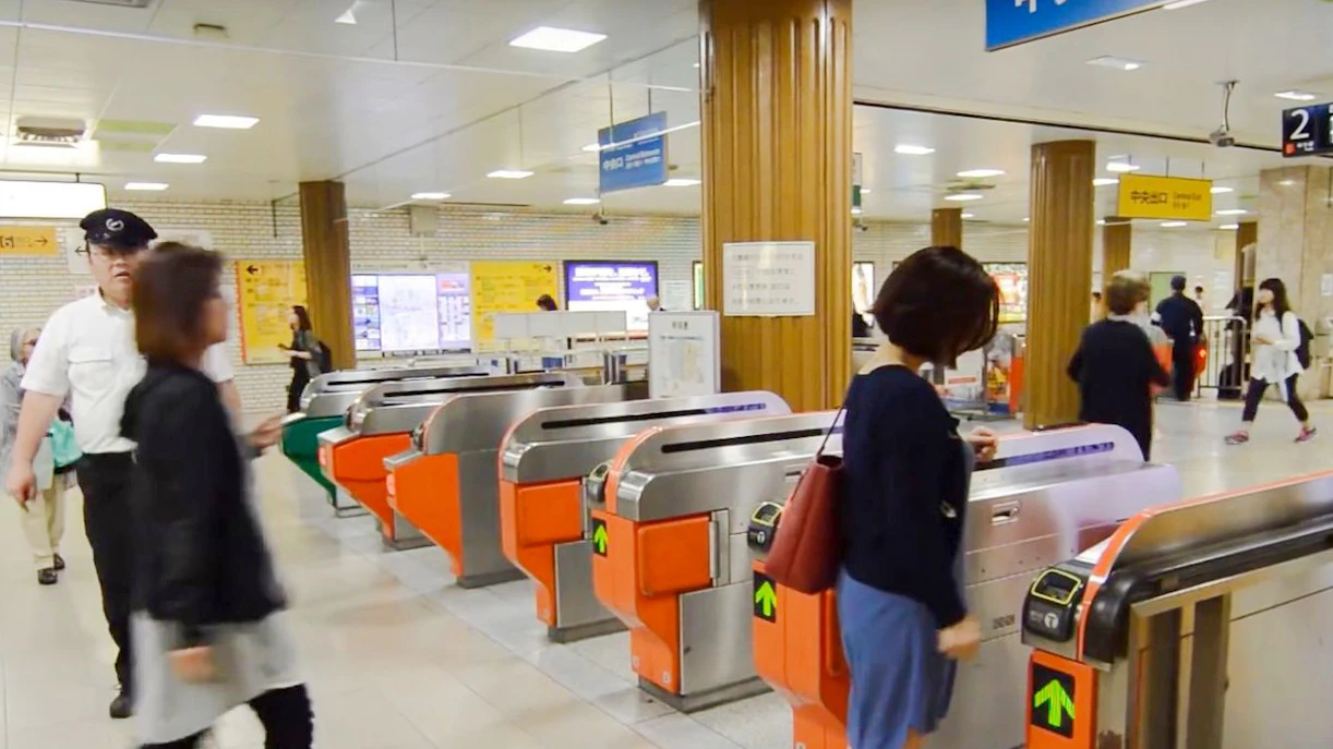 Fukuoka City subway turnstiles with passengers entering the station.
