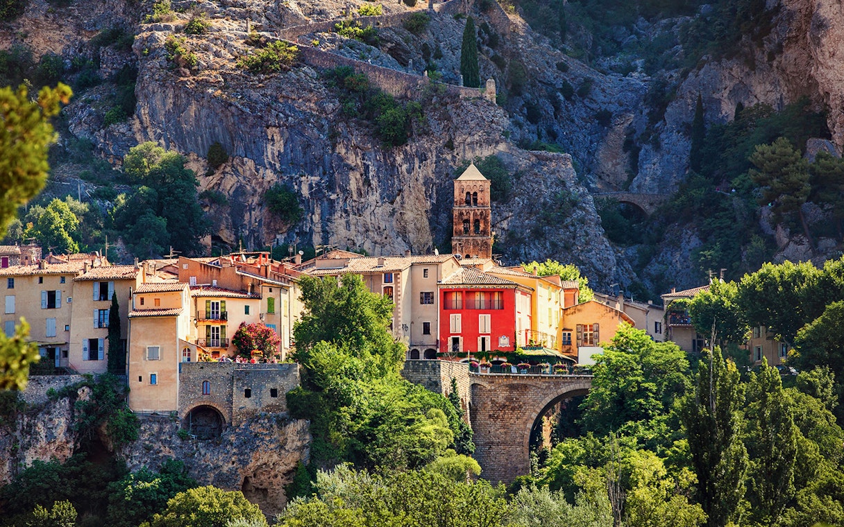 Moustiers Sainte Marie village with colorful buildings and church tower against rocky cliffs.