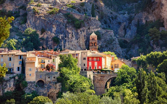 Moustiers Sainte Marie village with colorful buildings and church tower against rocky cliffs.