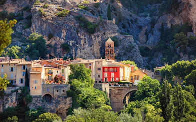 Moustiers Sainte Marie village with colorful buildings and church tower against rocky cliffs.