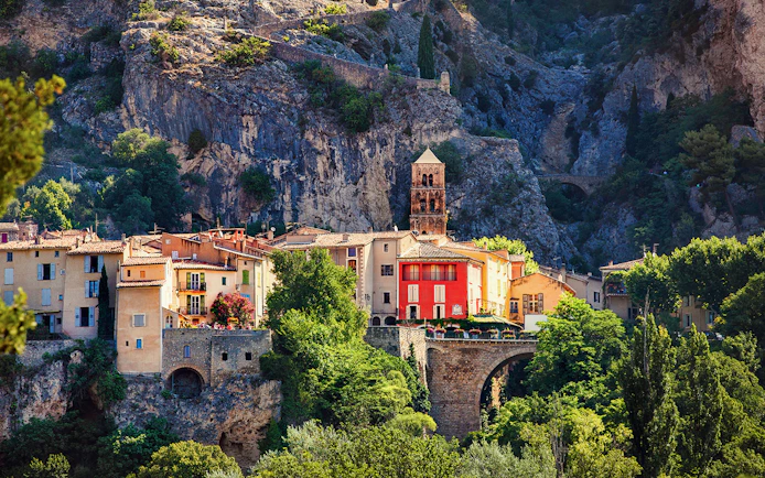 Moustiers Sainte Marie village with colorful buildings and church tower against rocky cliffs.