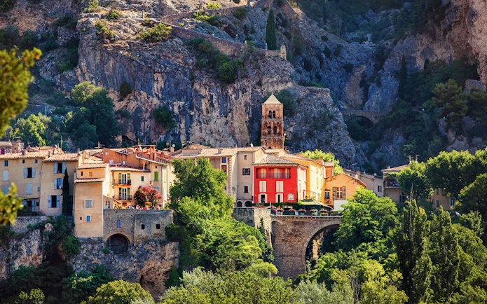 Moustiers Sainte Marie village with colorful buildings and church tower against rocky cliffs.