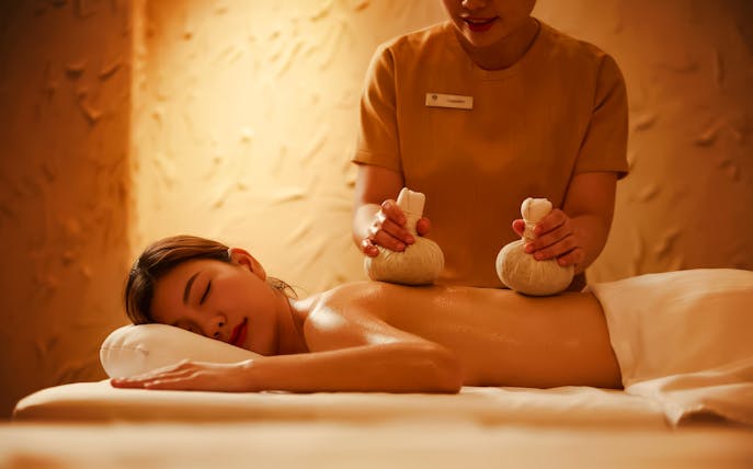Thai massage with herbal compress on a comfortable bed under ambient lighting.