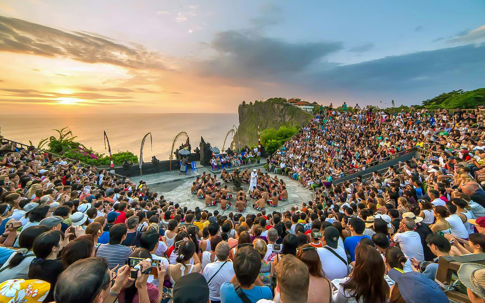 Open-air Kecak dance performance at Uluwatu Temple, Bali, with ocean sunset backdrop.