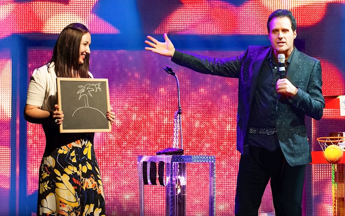 Performer on stage with a participant holding a drawing during The Mentalist show.