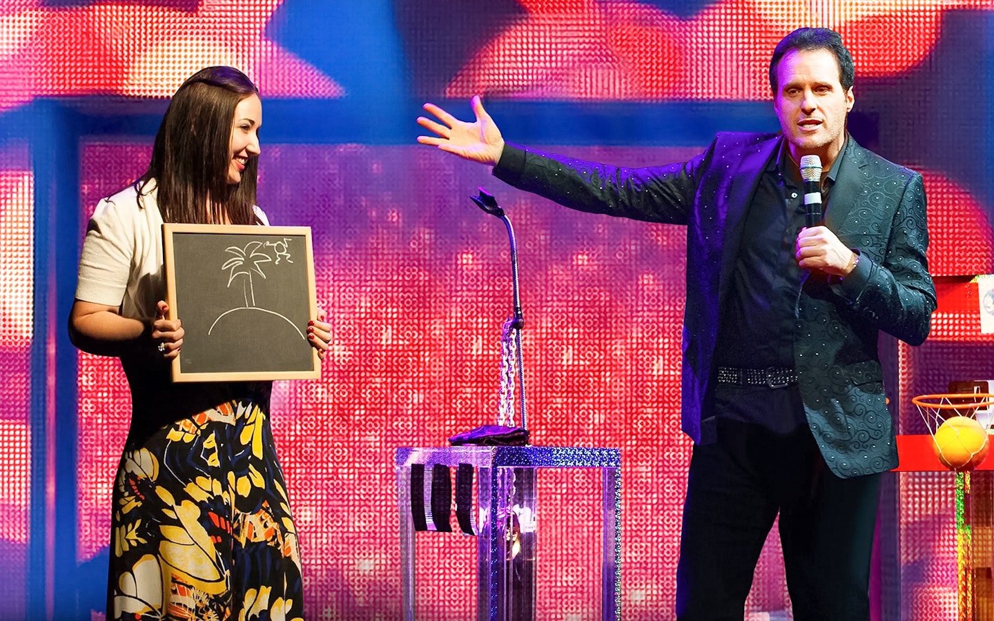 Performer on stage with a participant holding a drawing during The Mentalist show.