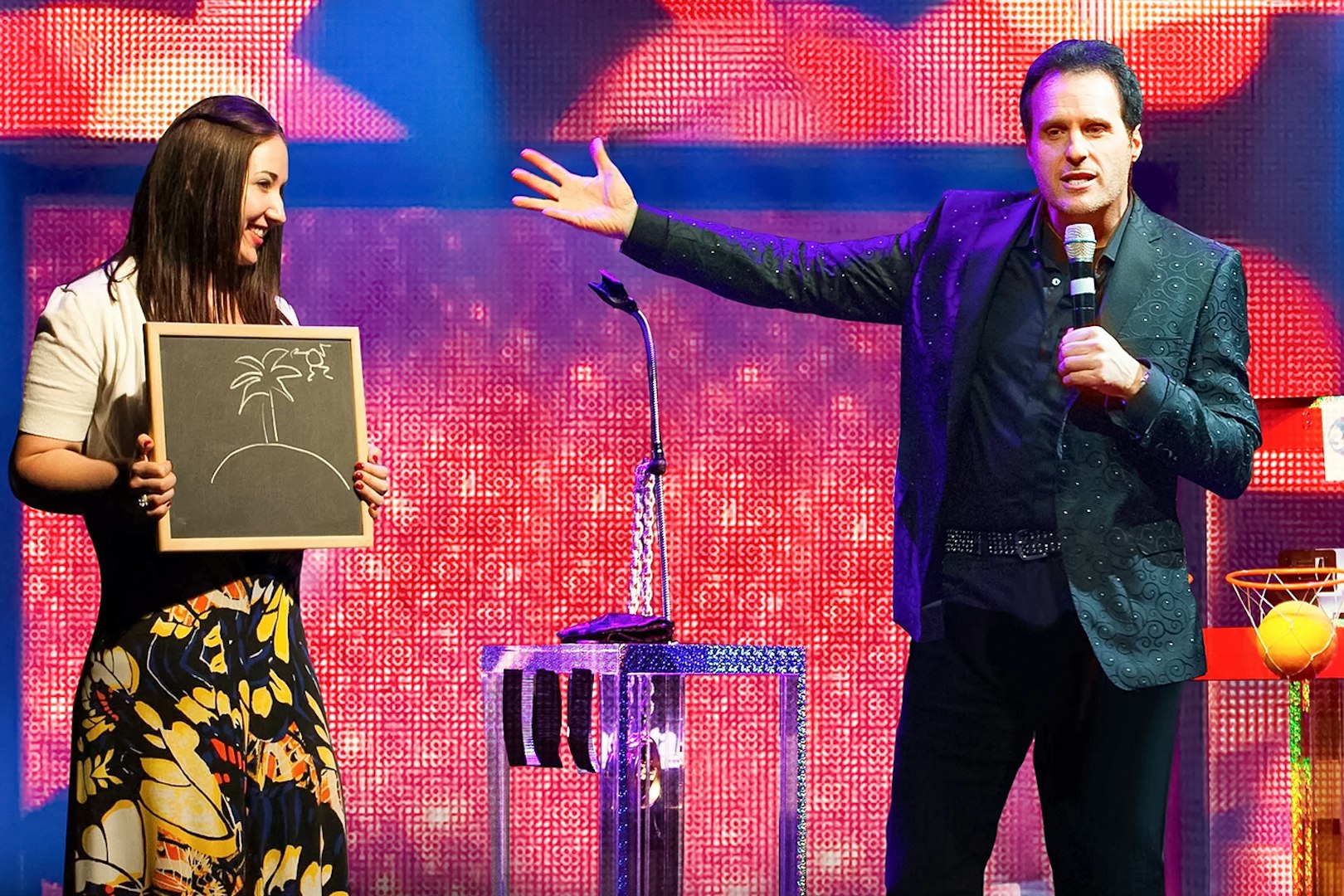 Performer on stage with a participant holding a drawing during The Mentalist show.