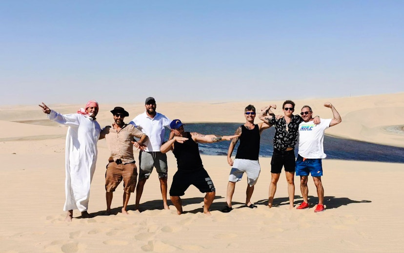 Group enjoying a half-day desert safari with sand dunes and a small oasis in the background.