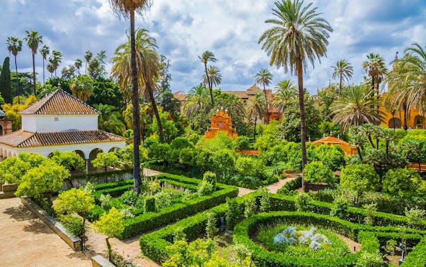 Gardens of Alcázar in Seville with palm trees, hedges, and historic architecture.