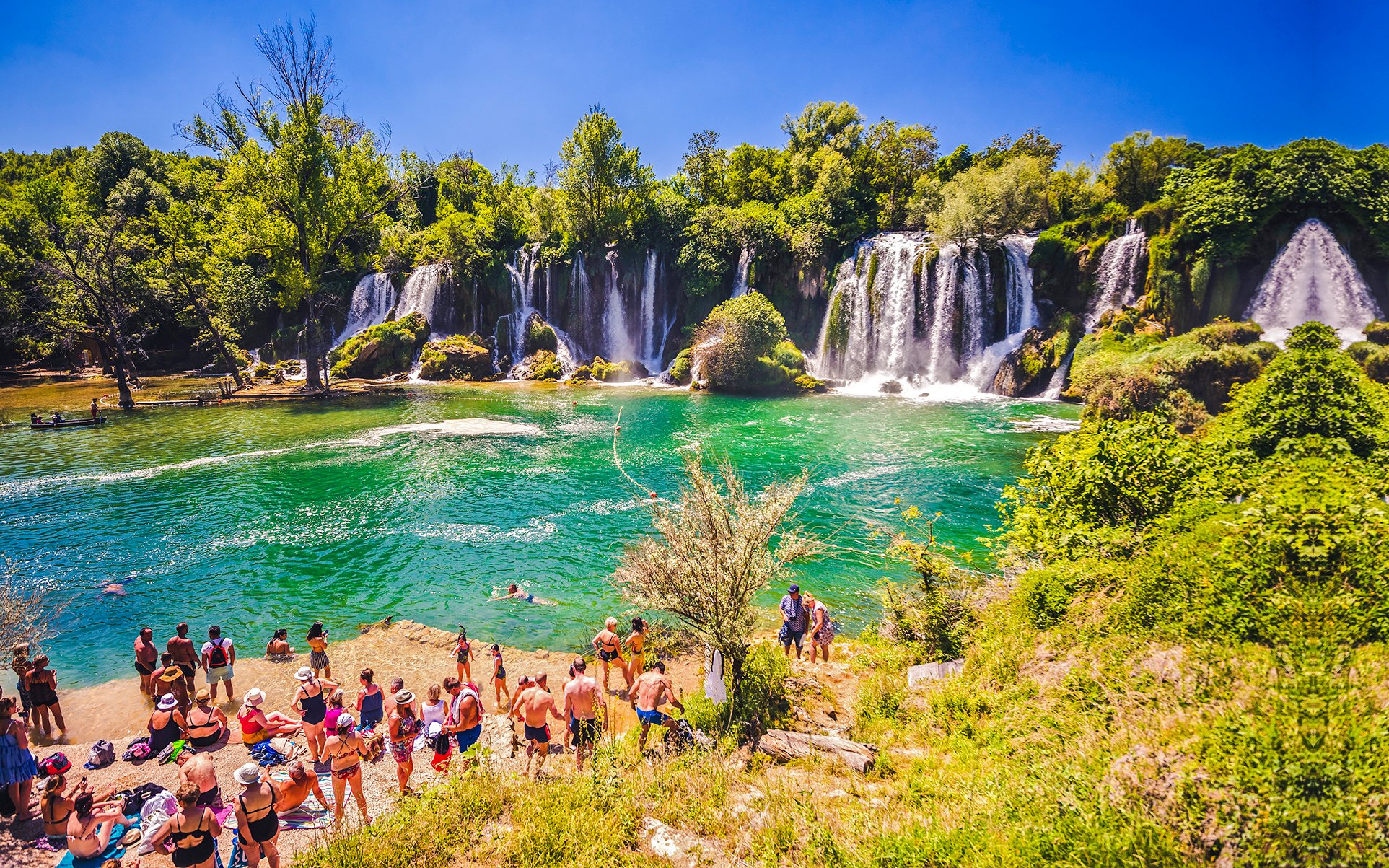 Visitors enjoying Kravica Waterfalls, lush greenery, and clear water near Dubrovnik.