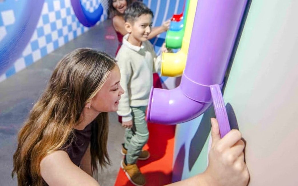 Children interacting with colorful tubes at Mind Games - Art Alive! exhibit.