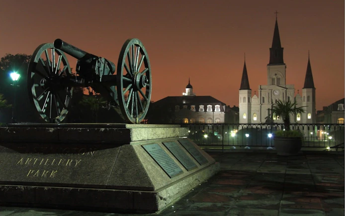 Cannon at Washington Artillery Park with St. Louis Cathedral in New Orleans at dusk.
