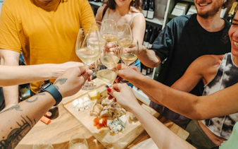 Toasting with wine glasses over a cheese and charcuterie board on the Ultimate Paris Food Tour.